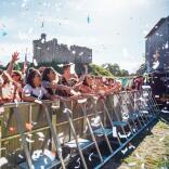 Audience at a music gig in Tafwyl standing behind a barrier with confetti in the foreground and Cardiff Castle in the background
