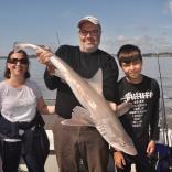 Two adults and a child on a boat hold up a 14lb starry smoothound fish.