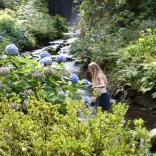 Two people crossing a stream on stepping stones in ornamental gardens.