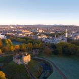 drone footage looking down onto Cardiff Castle with green grass and city view in far distance 