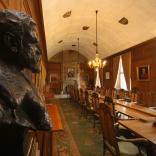 The council chamber witha   head statue of a man low chandelier lights over a log table with fireplace at the end.