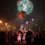 Crowd watch a giant peach in the sky against a back drop of fire works