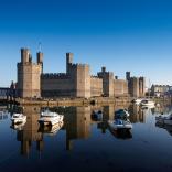 Exterior view of Caernarfon Castle from the South with boats and water.