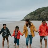 A family (mother and three children) on Pendine Beach, West Wales, holding hands and smiling.