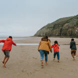 Eine Erwachsene und drei Kinder rennen an einem Strand.