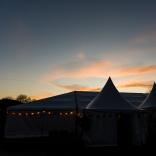 A tent with fair lights and a sunset in the background.