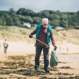 A man on a beach using a litter picking grabber tool to collect litter.