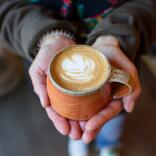 Two hands holding a freshly made milky coffee.