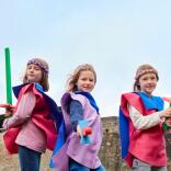 Three children dressed as knights within castle walls.