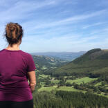 A woman in a purple walking top looking down onto a green valley.