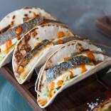 Three tacos filled with fish and lettuce and drizzled with an orange sauce. 
