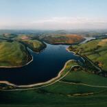 Overhead panorama of a glassy reservoir and sundrenched green hills