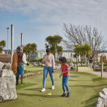 Mum and son play crazy golf on a sunny day whilst dad and daughter watch 