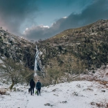 people walking dogs in snow with waterfall in background.