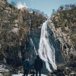 people and dogs in snow with waterfall in background.