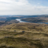 Views from a mountain top looking over green moorland and lakes.
