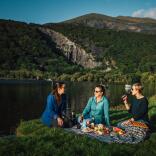 three woman having a picnic by lake.