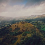 Drone shot of a ruined castle on a grassy hill.
