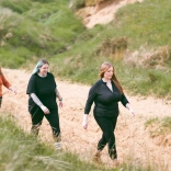 Tri pherson yn cerdded trwy dwyni tywod. 