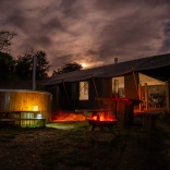 Night image of a glamping cabin, with a hot tub and lit firepit outside.