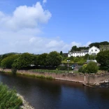 A large white hotel and castle overlooking a river, with a promenade alongside.