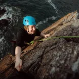 smiling climber wearing helmet climbing sea cliff.