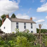 A large, white-washed cottage next to a flower garden. 
