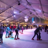 ice skaters in covered outdoor rink with coloured lights.