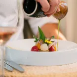 A small plate of food being drizzled with dressing at a restaurant.
