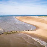 A short, white-painted lighthouse on a beach backed by grassy dunes.