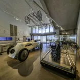 Interior of the Museum of Land Speed in Pendine, showing the historic 'Babs' racing car and engine displays in a bright gallery.