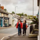 Two ladies walking along a shop filled street.