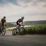 Road cyclists cycling uphill through rolling green hills with a lake visible in the background