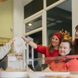 Customers collecting a bag of Welshcakes at a bakery counter while staff serve behind the display.