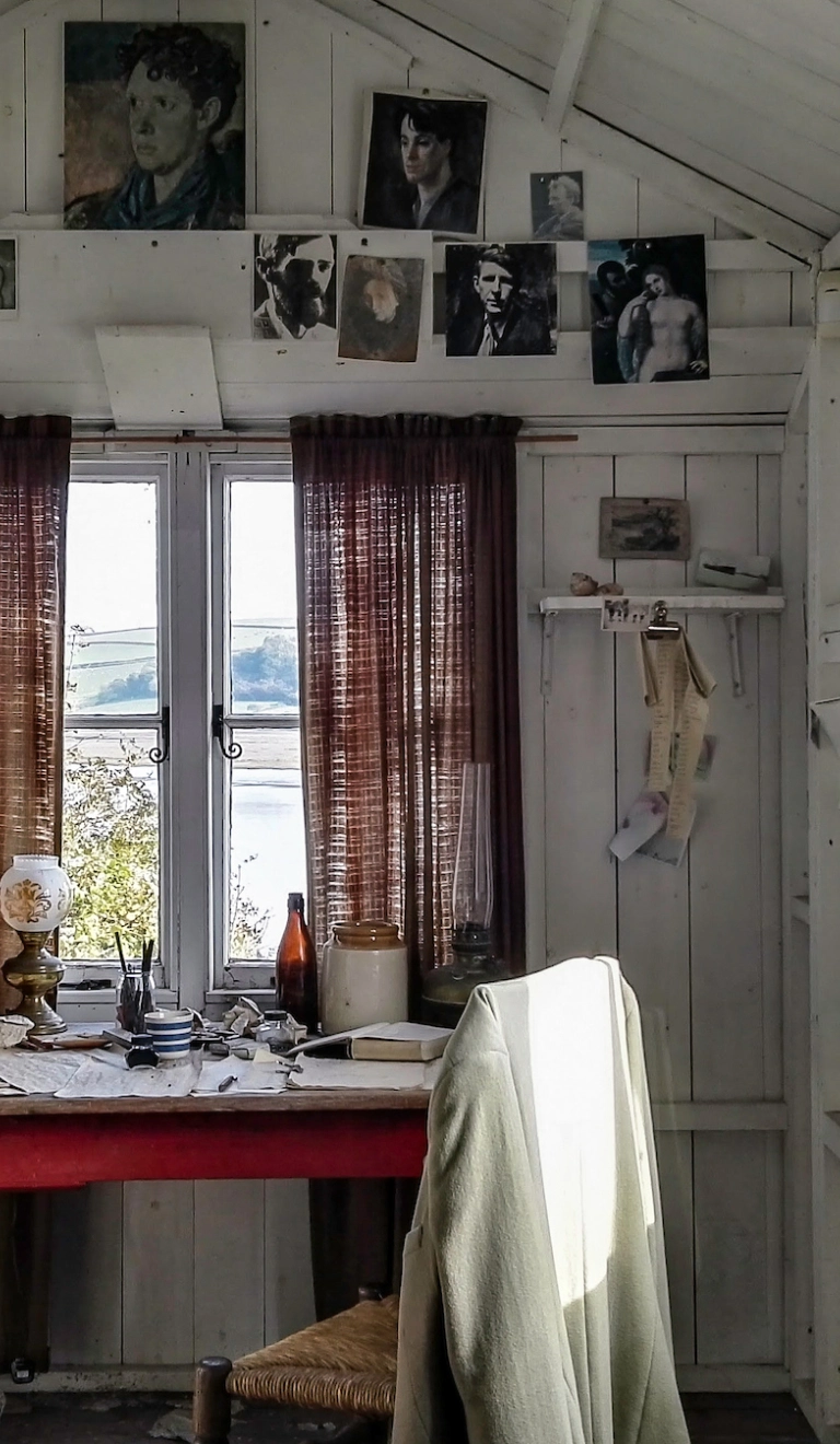 An inside scene of a shed with a writing desk and photographs on the wall.
