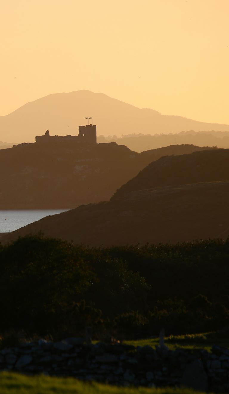 Criccieth castle, silhouetted against a pale orange sky