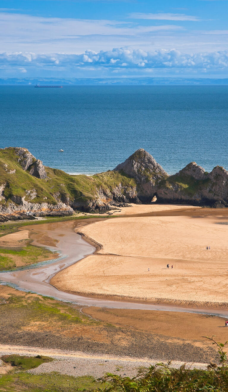 Tide out at Three Cliffs Bay with rivulets of sea water left on the sandy beach.