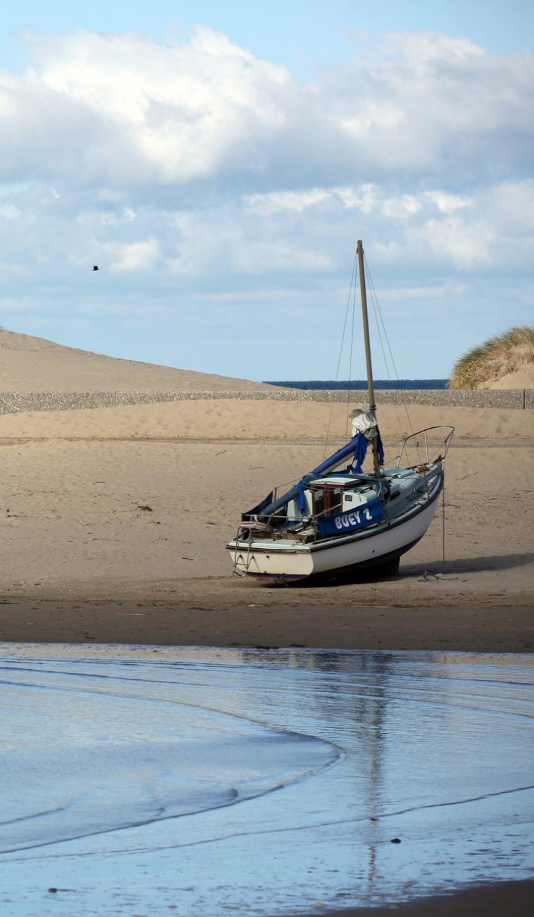 Couple walking on Barmouth beach with a boat on the beach