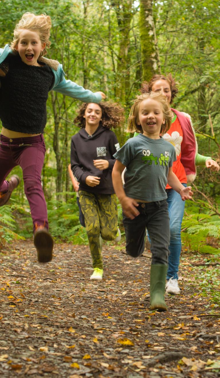 Four children running in woodland.