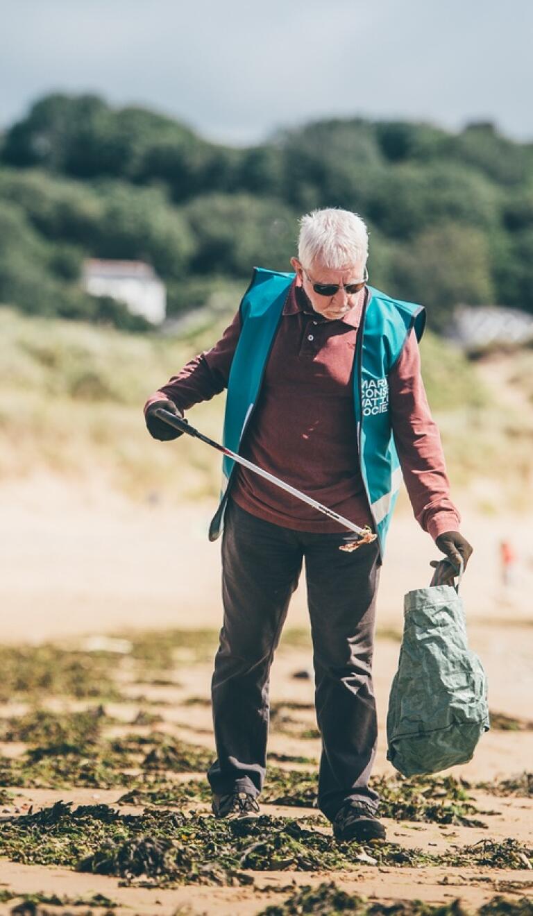 A man on a beach using a litter picking grabber tool to collect litter.