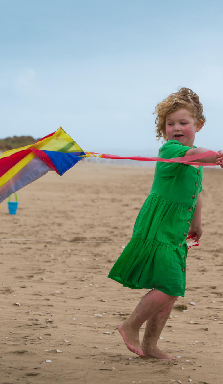 A girl flying a kite on a sandy beach.