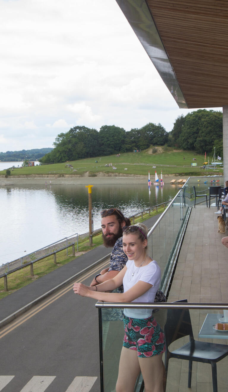 A couple stood in visitor centre looking out over a lake.