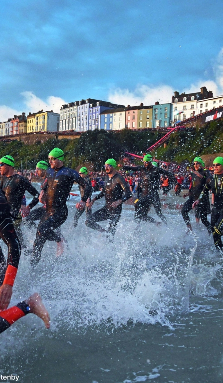 Many swimmers wearing green caps running into the sea.