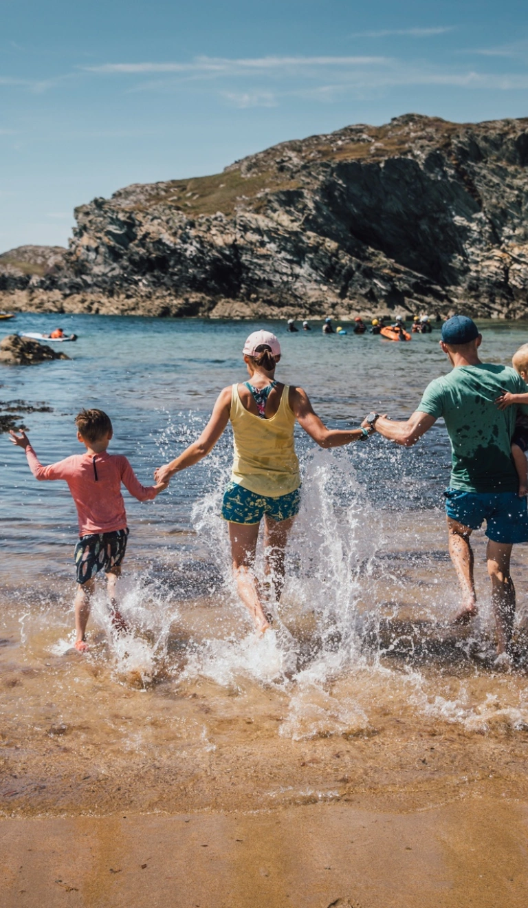 Two adults, and two children running into the sea on a sandy beach on a sunny day.