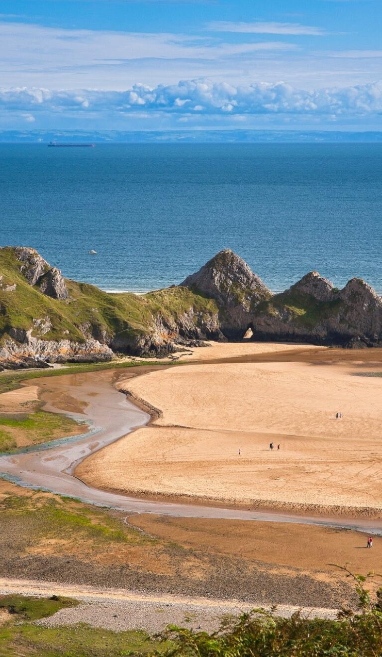 Tide out at Three Cliffs Bay with rivulets of sea water left on the sandy beach.