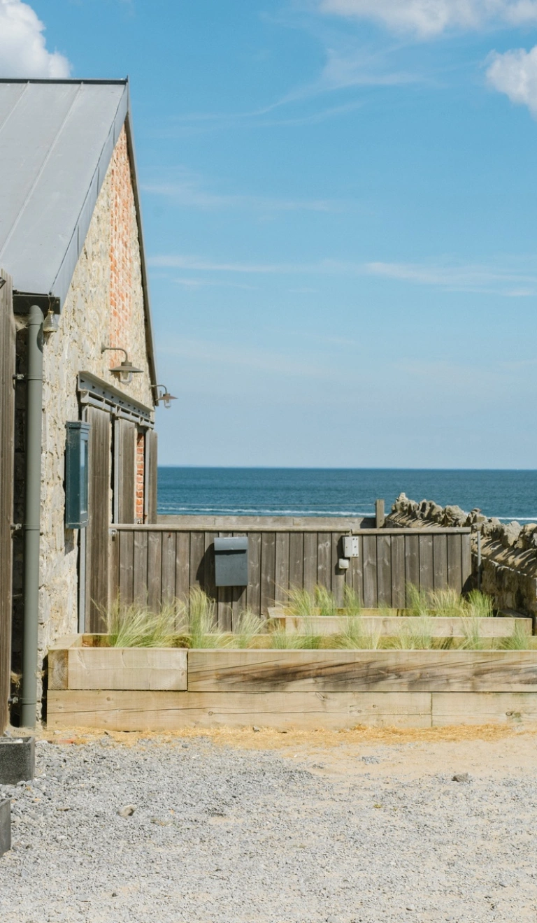 Tu allan bwyty Beach House yng Ngŵyr gyda'r môr yn y cefndir.