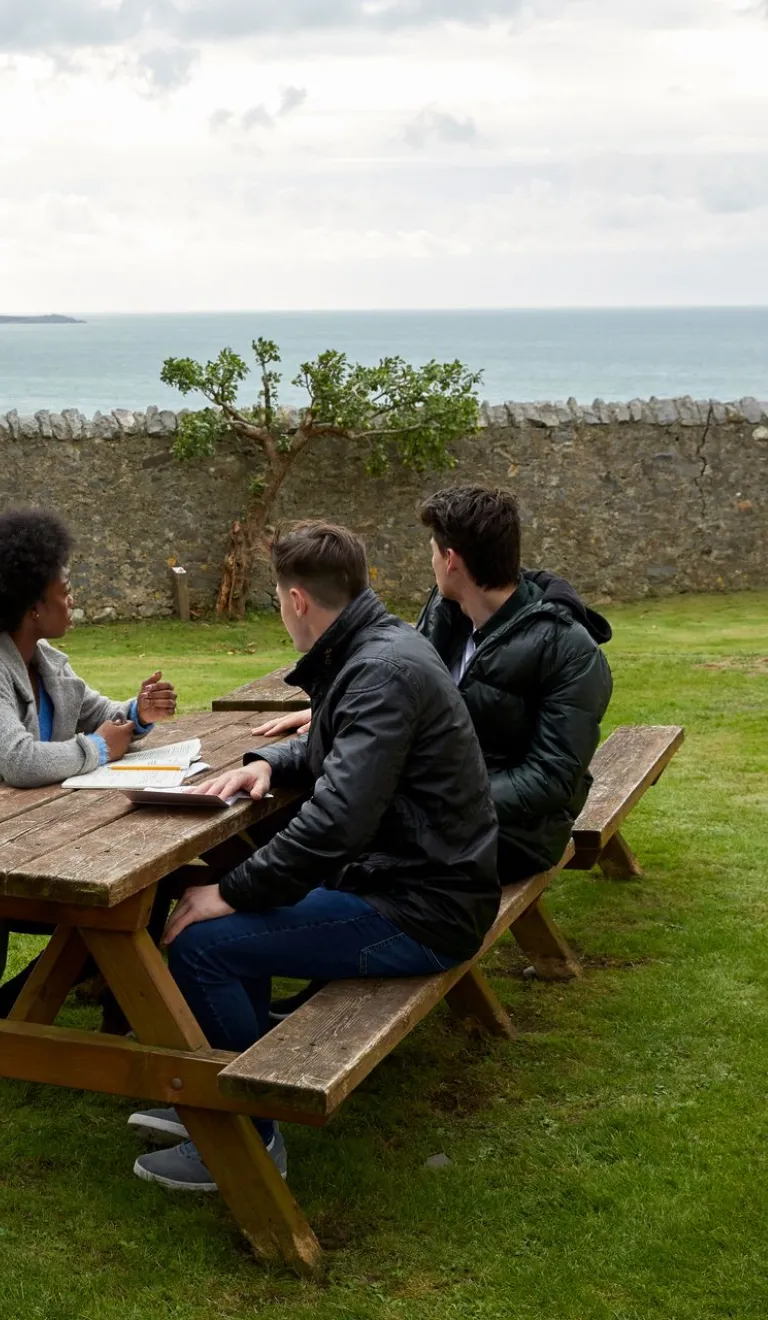three people sat at bench with views of the sea.