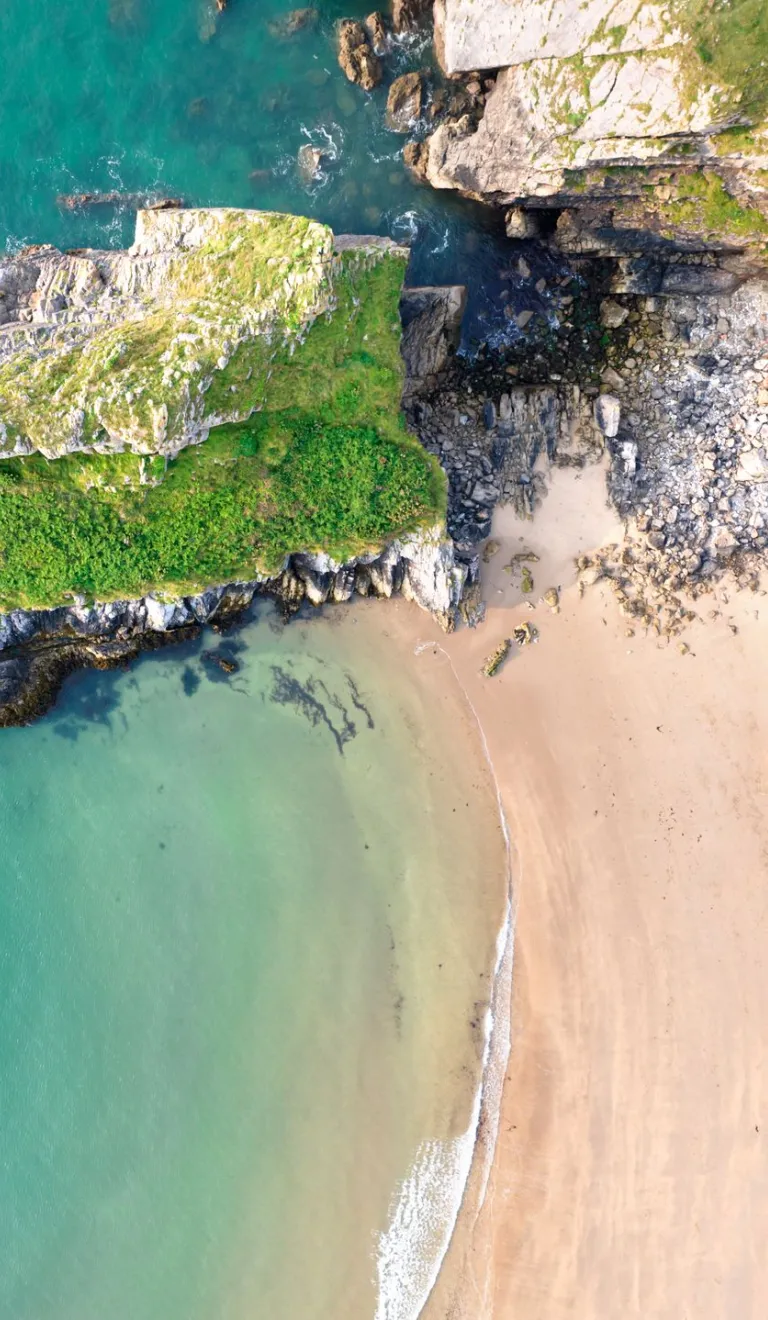 A golden sand beach with a rocky outcrop jutting into a  turquoise sea. 