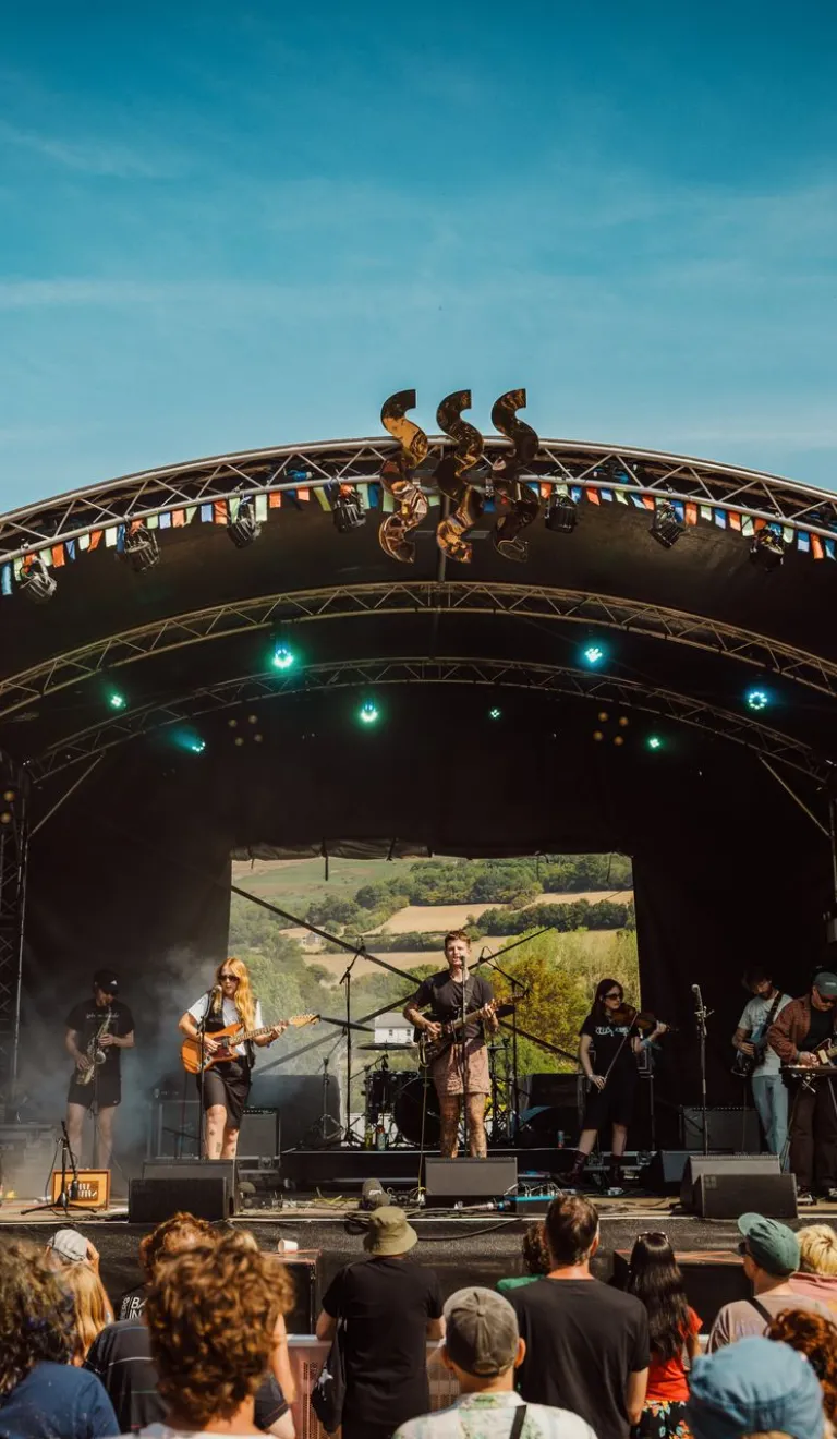 band playing at festival on a sunny day with crowd watching and hills in background.
