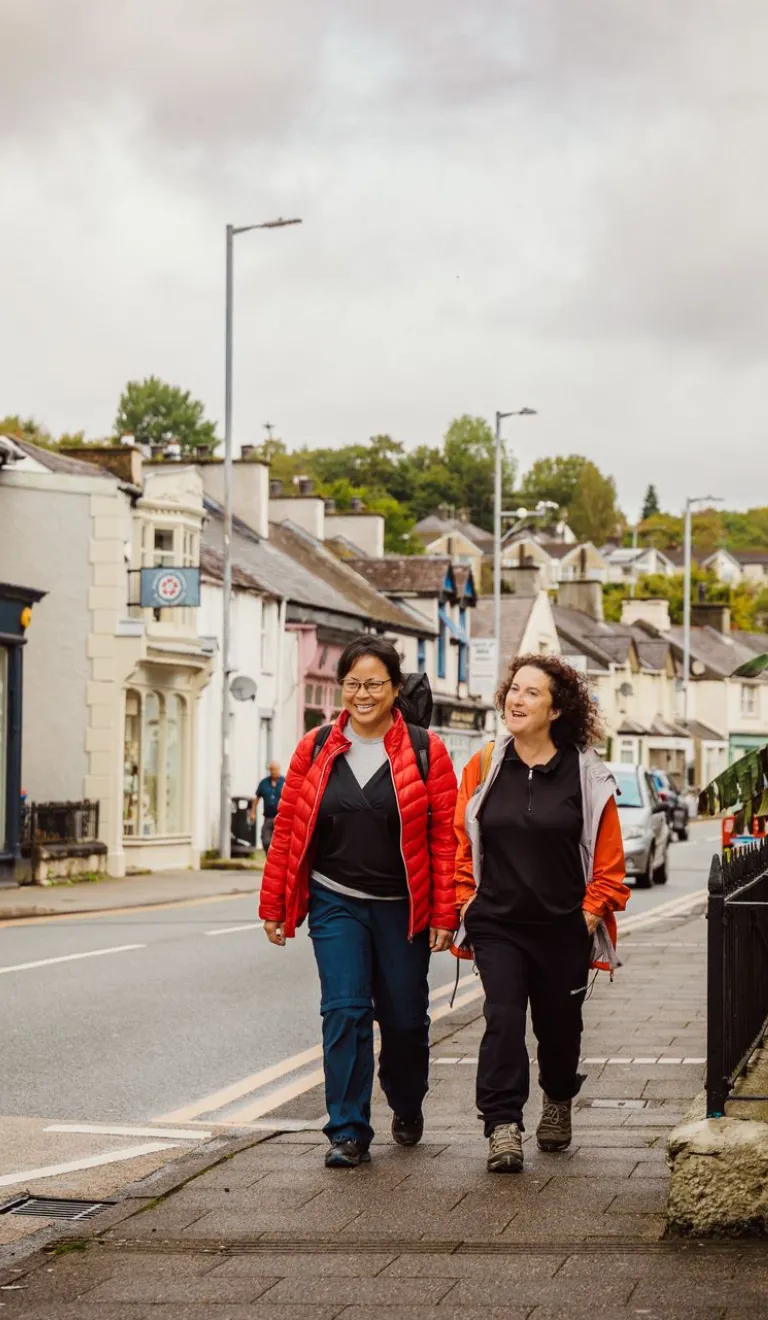 Two ladies walking along a shop filled street.